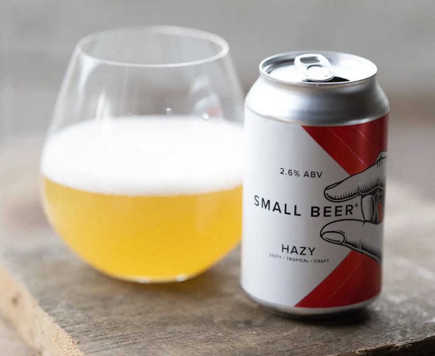 Can of Small Beer hazy craft beer beside a glass on a wooden table.